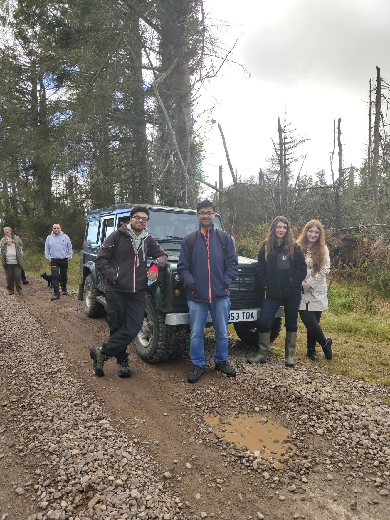 four NICD trainees leaning on a car in Northumberland on a project visit